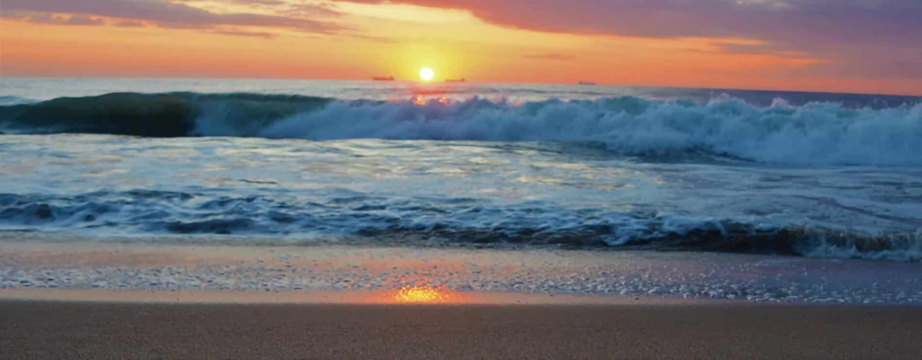 Beautiful pink and gold sunset over the waves of the ocean on the sandy shore.