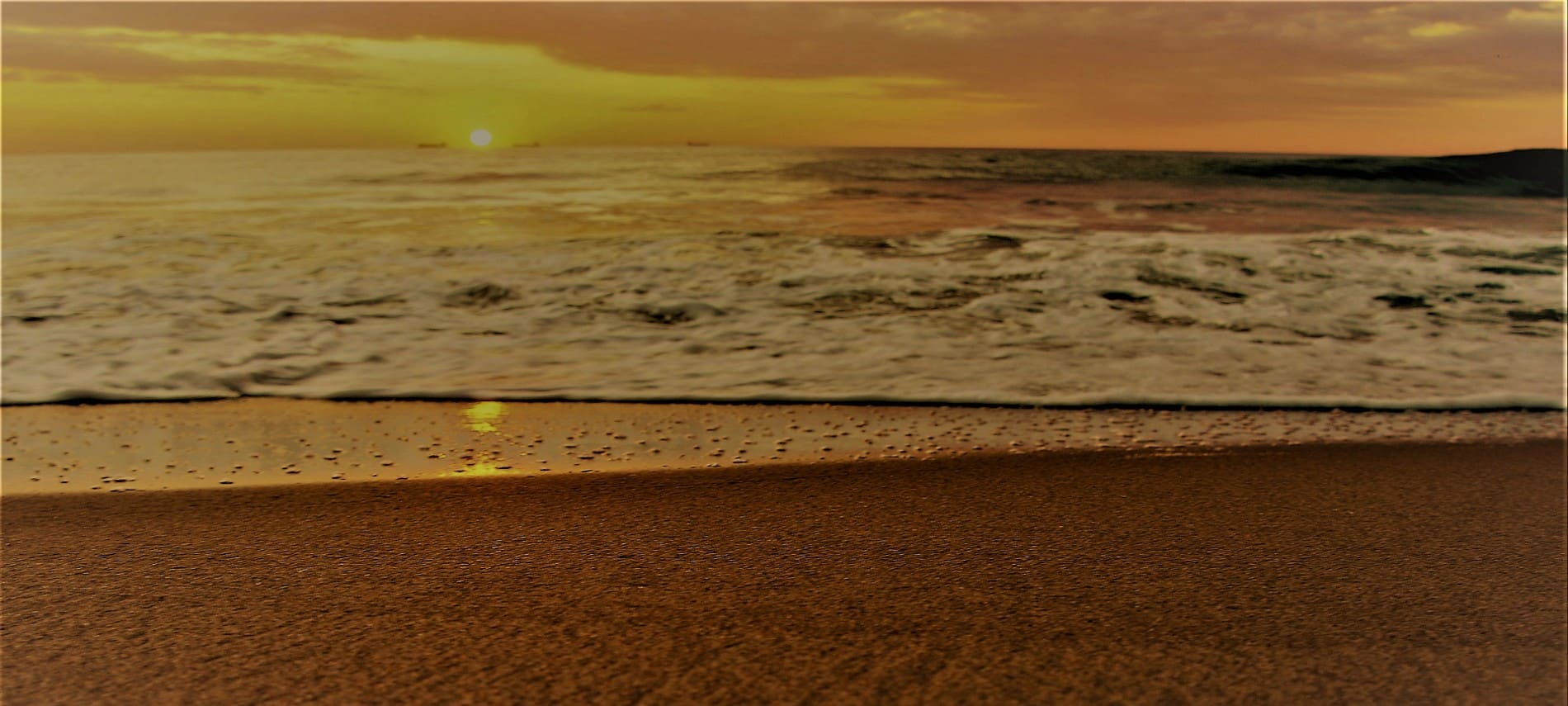 Ocean waves coming into the sandy shore of the beach at sunrise.