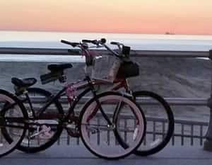 Two bikes on a boardwalk overlooking the beach at sunset.
