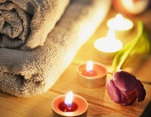 Tealight candles glow next to a purple tulip and stack of fluffy towels.