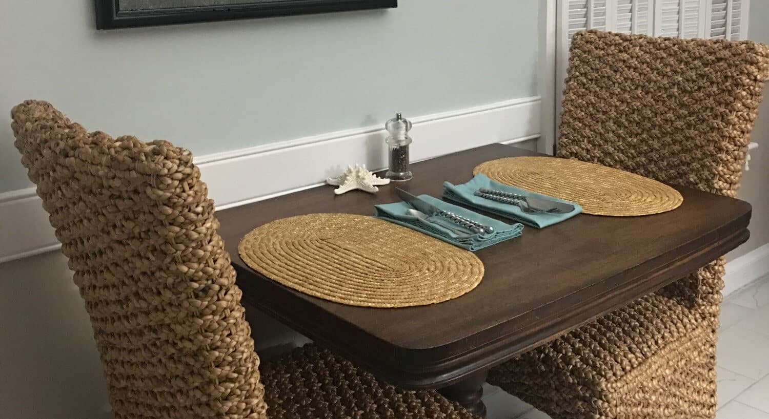 Table with wicker chairs  set for two  with placemats and cutlery. 