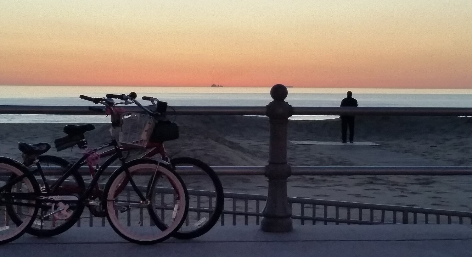 Two bikes on a boardwalk overlooking the beach at sunset. 