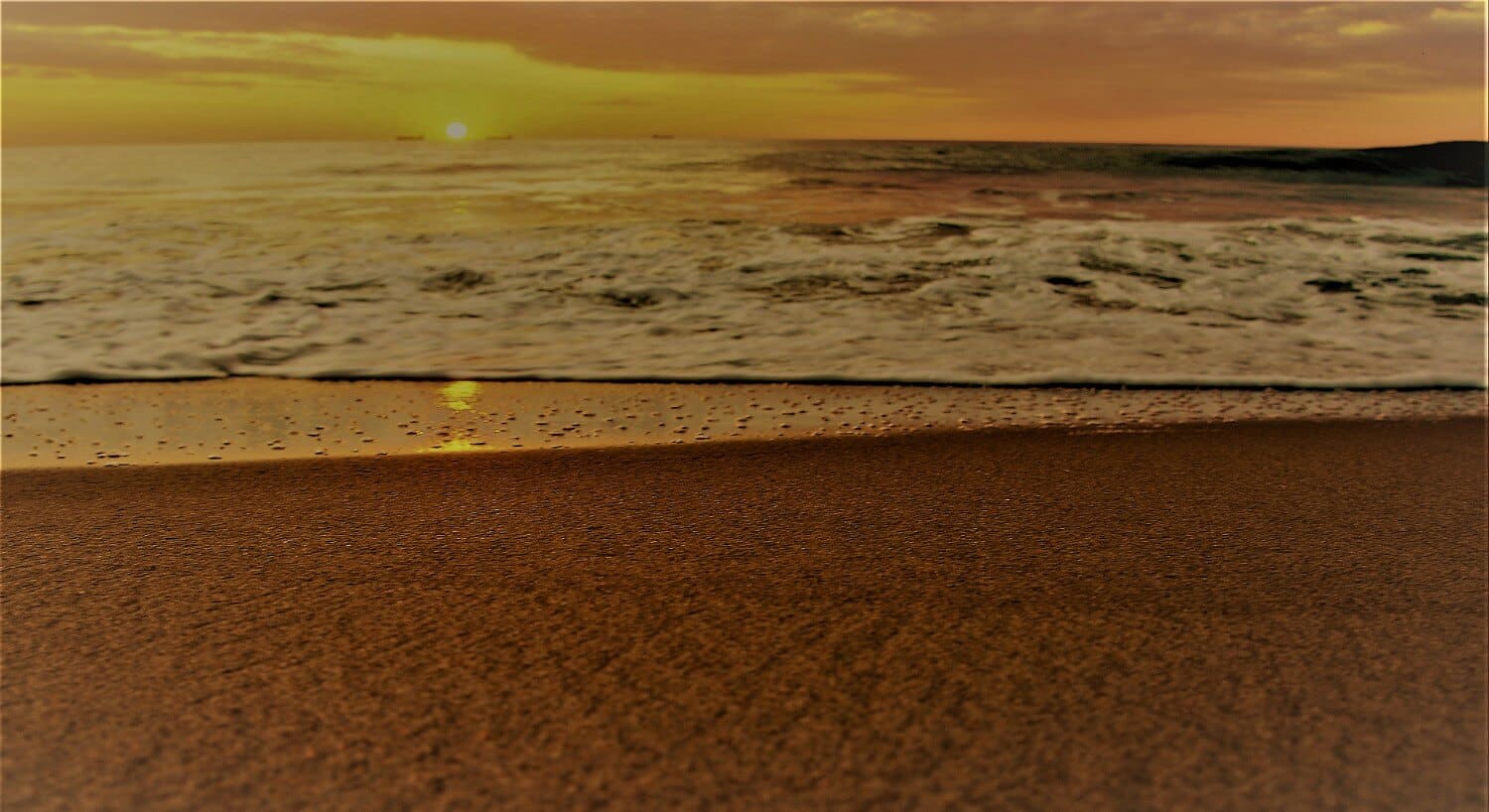 Ocean waves coming into the sandy shore of the beach at sunrise. 