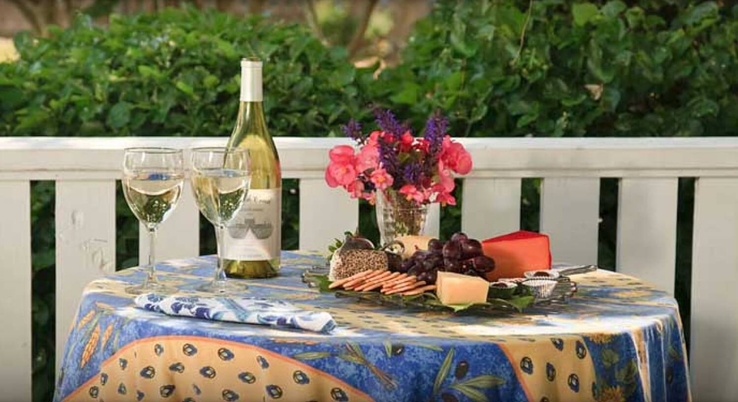 Bottle of white wine with glasses and a cheese tray on a covered table outdoors. 