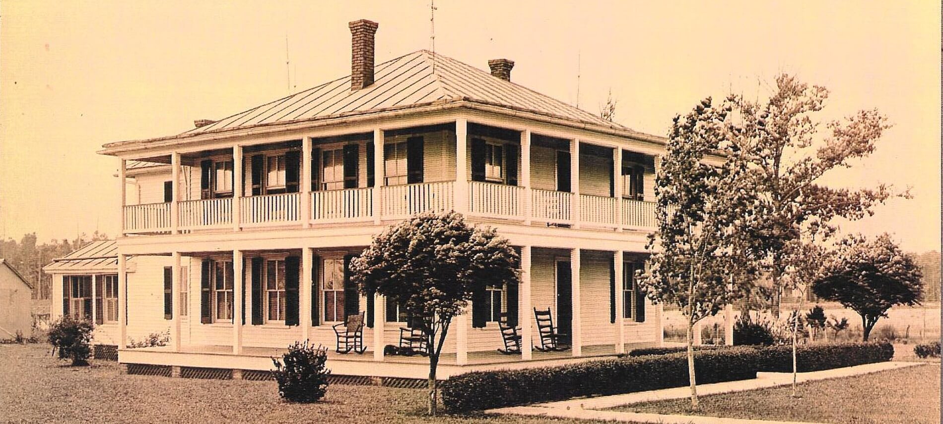 Sepia toned photo of Barclay Cottage Bed & Breakfast in past times- large white home with two-story wrapped porch.