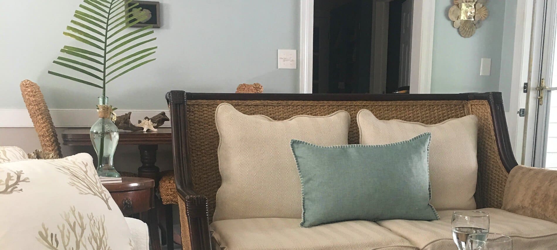 Wood and wicker sofa with tan and blue pillows in a seating area with a table holding wine.