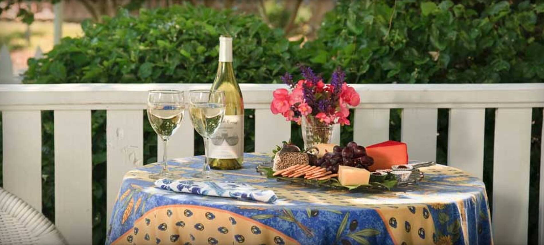 Bottle of white wine with glasses and a cheese tray on a covered table outdoors.