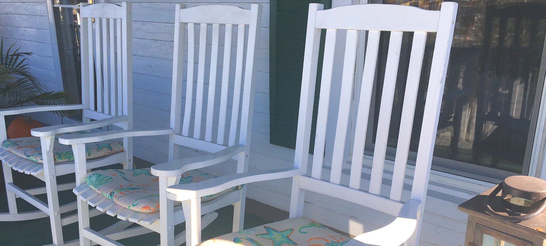  Row of white rocking chairs on a front porch. 