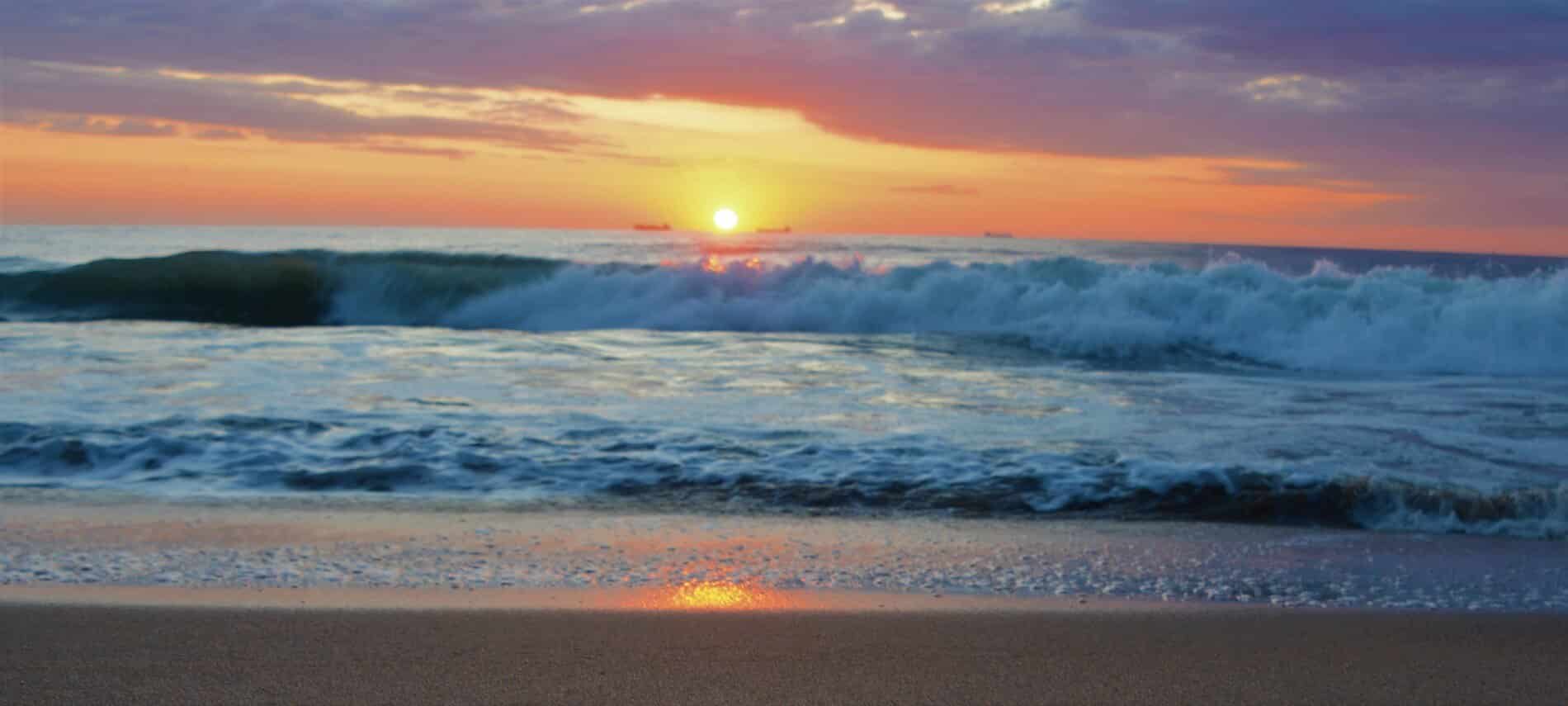 Beautiful pink and gold sunset over the waves of the ocean on the sandy shore.