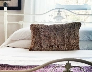 White iron bed with several pillows sits under a window with sheer curtains.