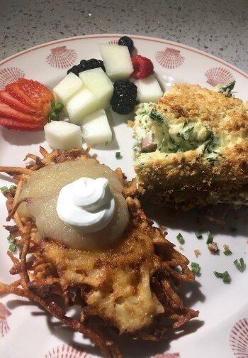 Breakfast plate with fruit, a potato pancake with applesauce and an egg dish.