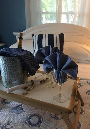 A tray with wine in a bucket and two wine glasses with blue napkins on a bed.