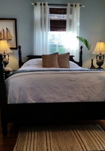 Large bed made up in white and tan between night stands with matching grecian urn lamps.