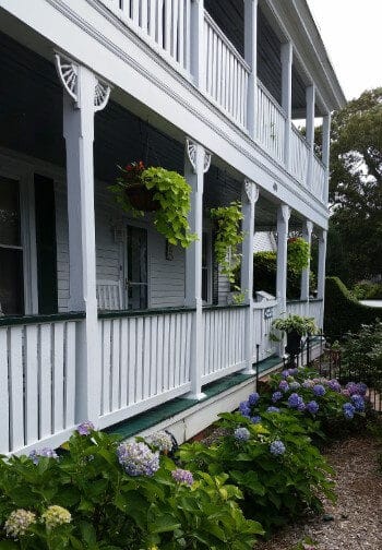A two-story porch fronted by masses of pink, white and lavender lilac bushes.