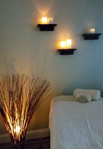 A massage table in a candle-lit room with a lighted branch floor piece.