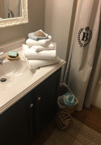 Stack of white towels and soap on the edge of a vanity sink next to a shower curtain with a B logo.